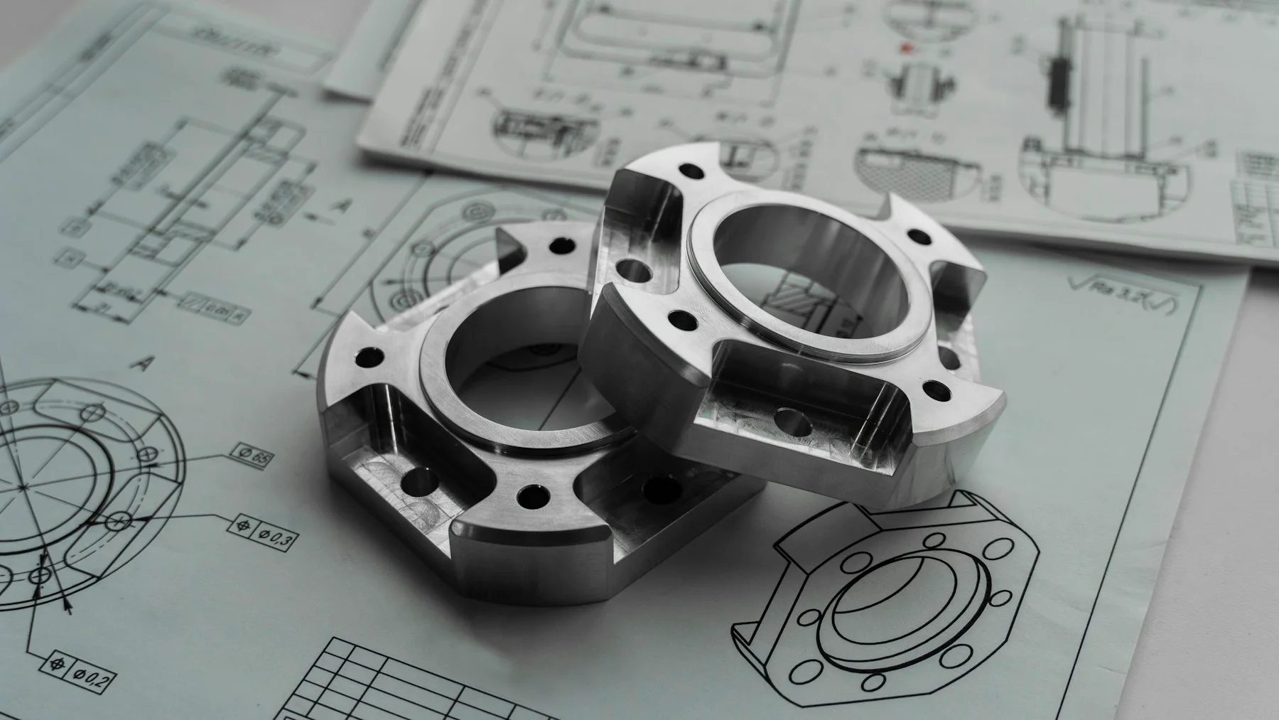 Machined metal components resting on their engineering drawings.
