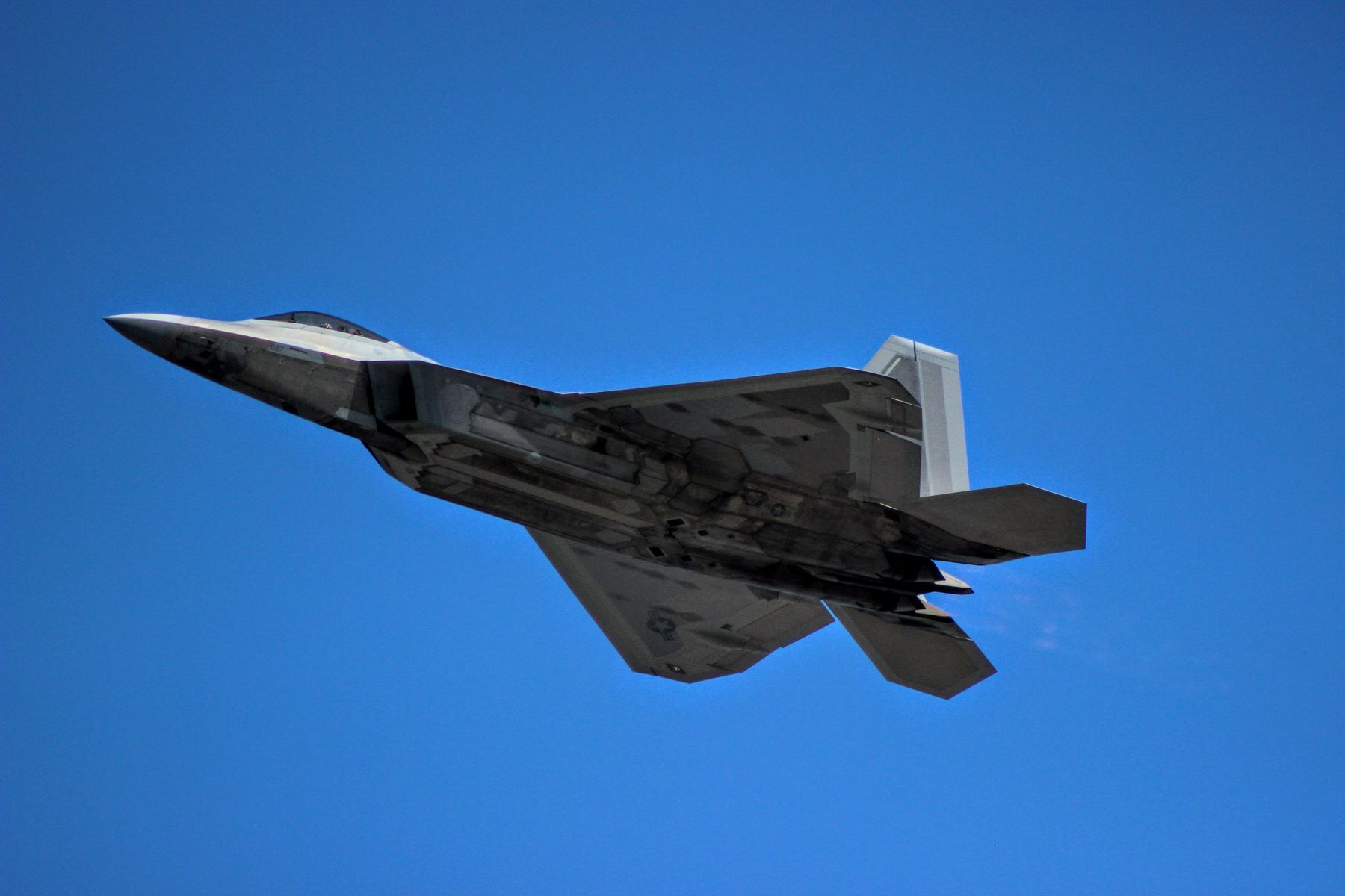 An F-22 fighter jet in flight against a clear blue sky.