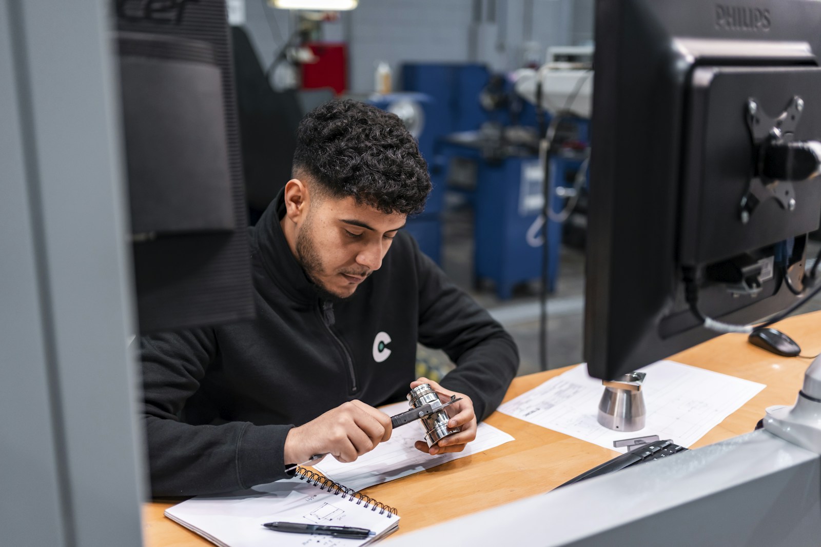 Technician measuring a machined component against its technical drawing.