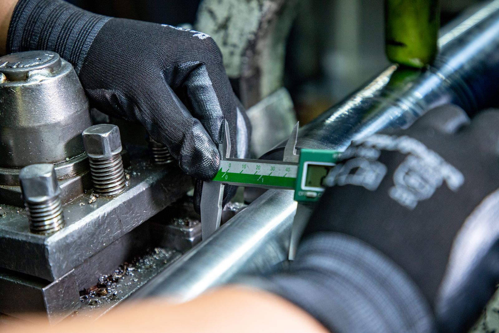 A machinist verifying the diameter of a finished shaft with a caliper.