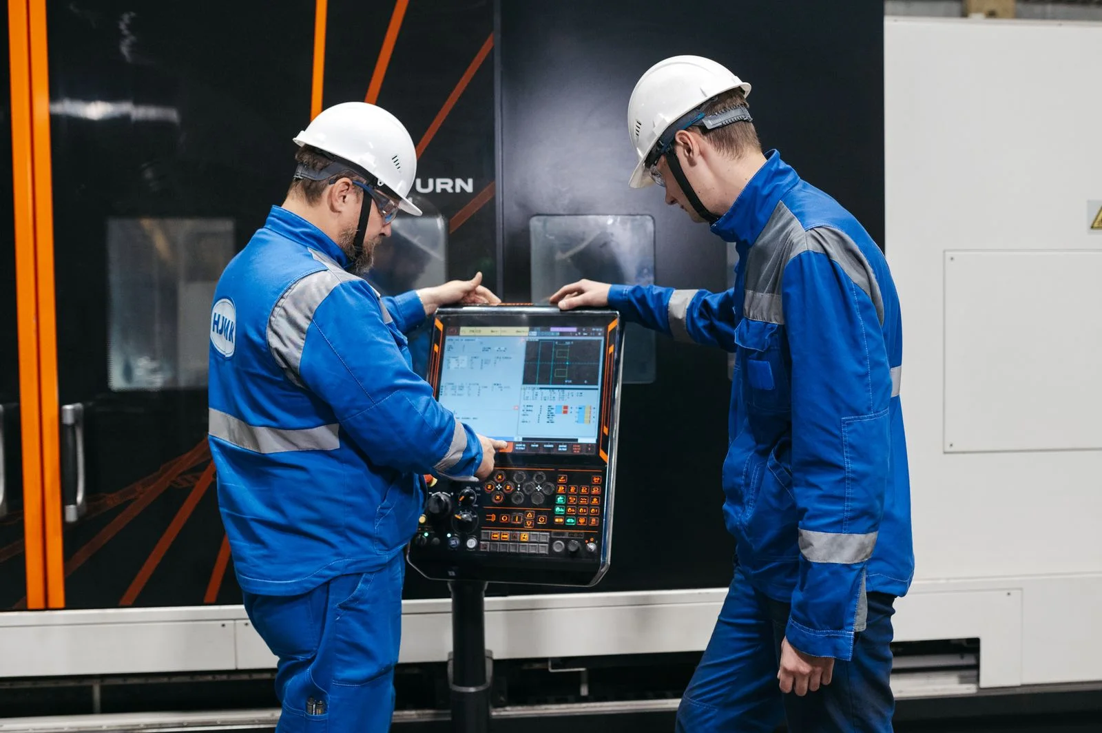 Technicians at an enclosed CNC machine’s control panel.