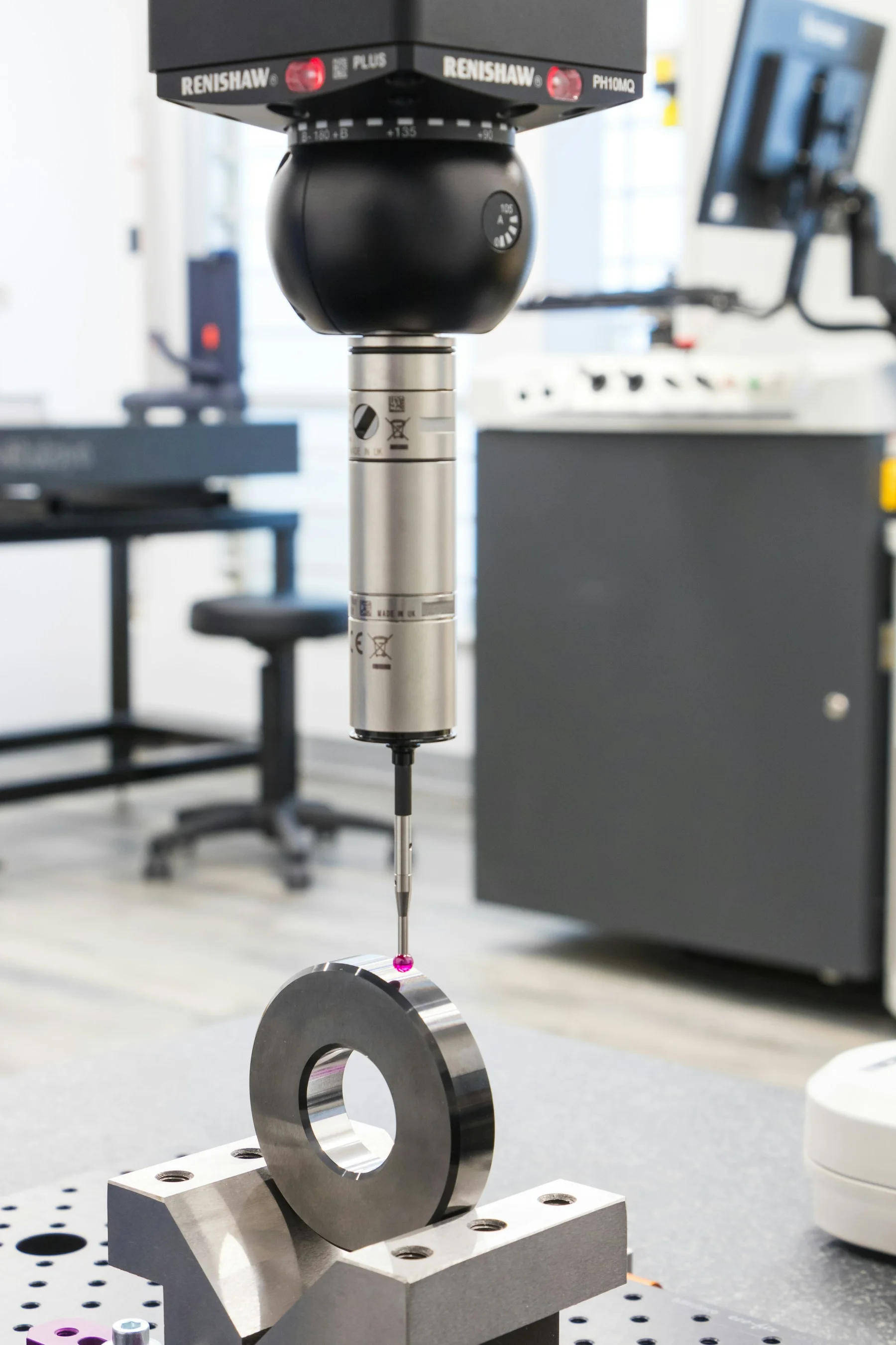 A coordinate-measuring probe checking a metal ring in a metrology lab.