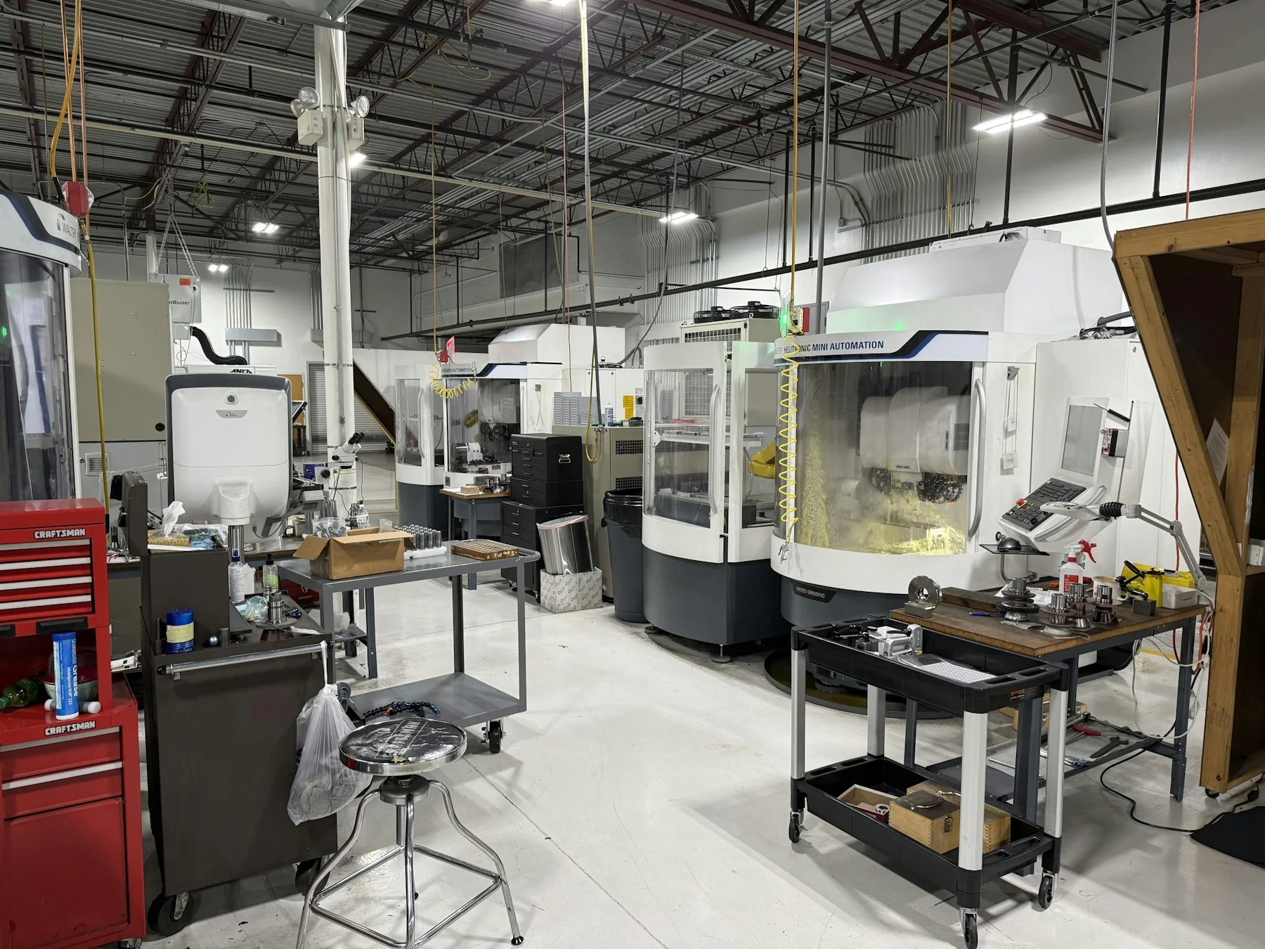A wide view of enclosed CNC machining centers, workbenches, and tooling across a machine-shop floor.